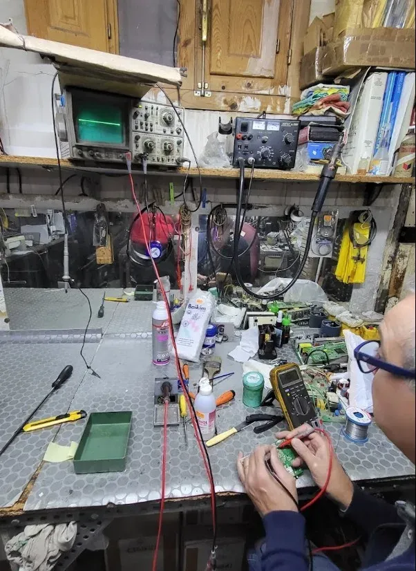 Banco de trabajo del taller con un osciloscopio, una fuente de alimentación y una placa en la mano.