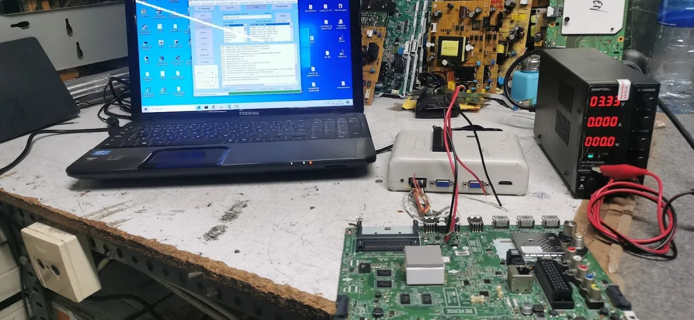 Banco de trabajo del taller con un portátil abierto, una fuente de alimentación de laboratorio y una placa grande